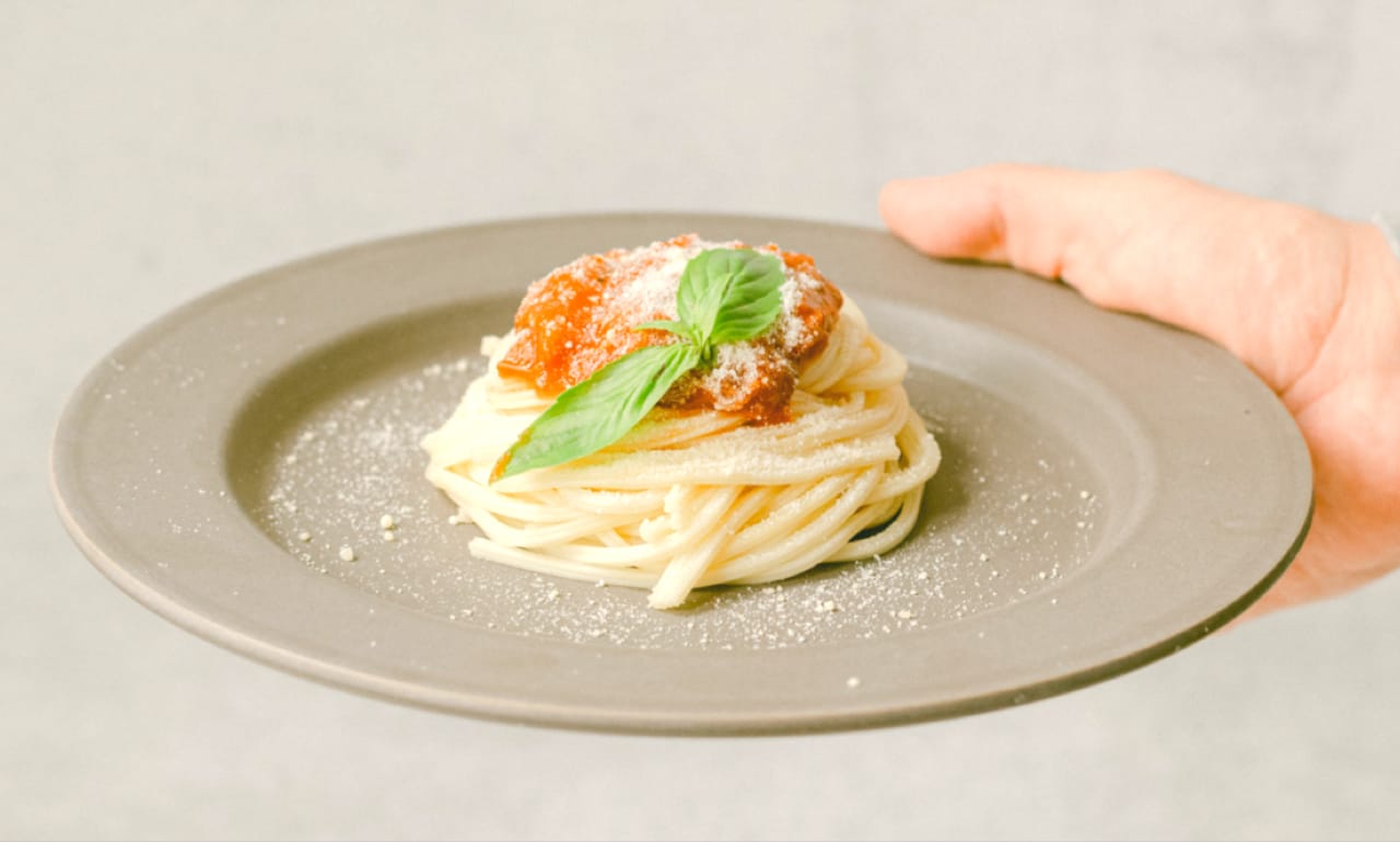 A hand holding a plate of spaghetti and mince