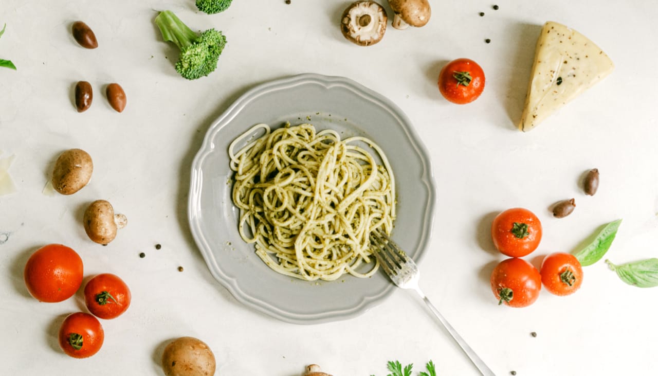 "Spaghetti on a plate, surrounded by  tomatoes, cheese, mushrooms, and broccoli
