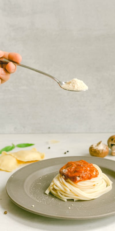 A spoonful of Parmesan cheese being sprinkled over a plate of spaghetti topped with mince sauce