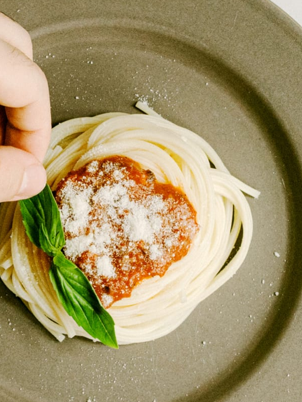 Person putting leave on plate of spaghetti bolognaise